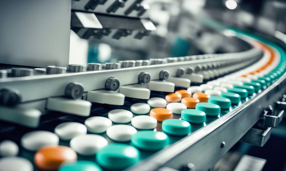 Several white, orange, and green pills on a machine in a factory moving down a conveyer belt for processing.