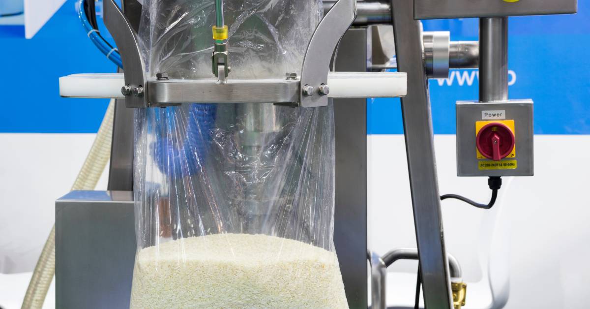 A packaging machine with tubes, wires, and buttons. A plastic bag is attached to it. The machine is filling the bag with rice.