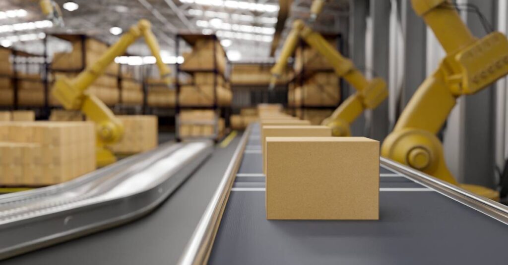 A conveyor belt in a warehouse moving boxes along, with yellow robotic arms completing tasks over them.