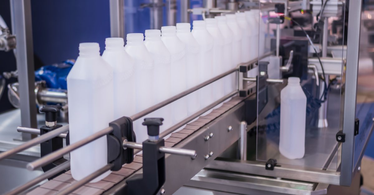 A line of plastic bottles moving down a conveyor belt on a manufacturing floor. They are ready to be filled with product.