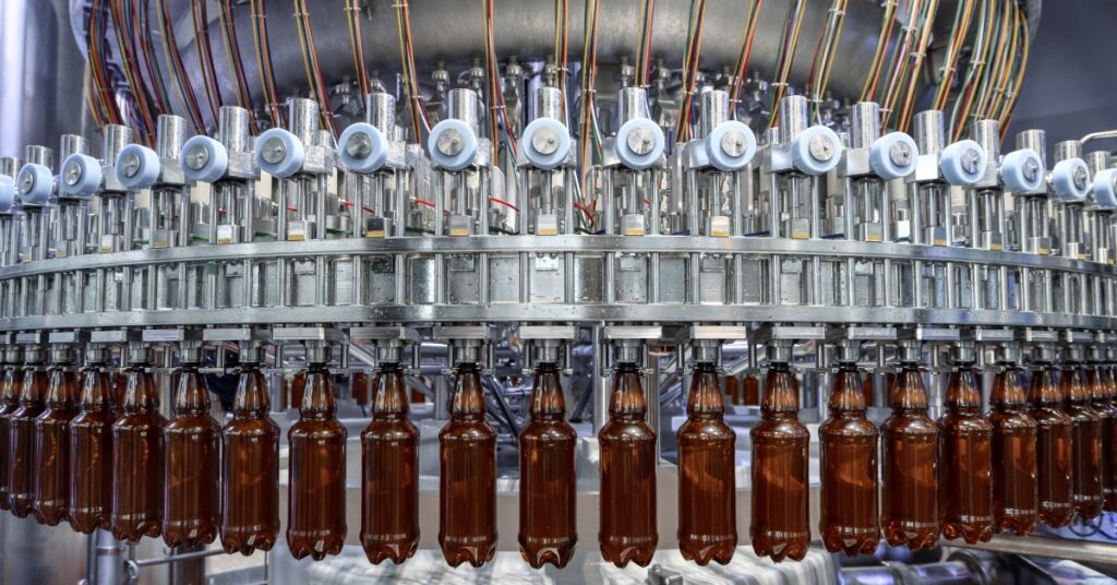 A filling machine on a manufacturing floor. The machine is holding a row of bottles that are ready to be filled with product.