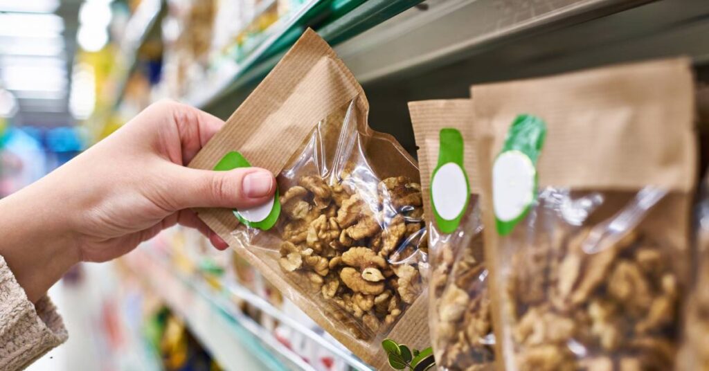  Fresh packages of walnuts on a shelf in a store with a hand reaching out to take one of them for purchase.