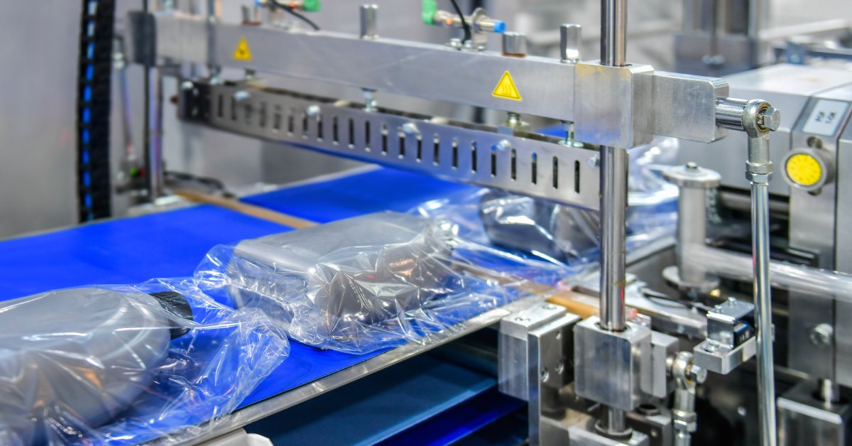 A blue conveyor belt on a machine with products moving down it. They’ve been sealed inside plastic packaging.