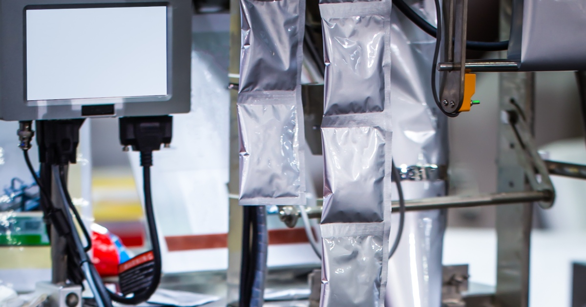 A long chain of empty pouches for food packaging being fed into a sealing machine on a manufacturing floor.