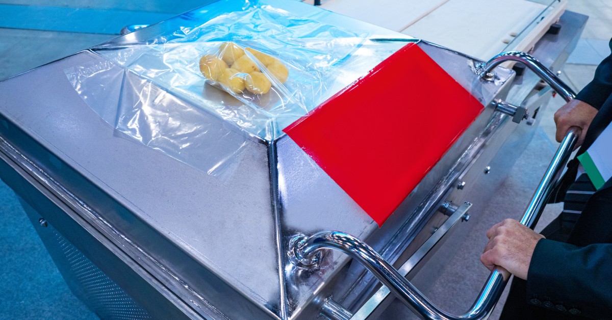 A worker in a manufacturing plant using an industrial machine to seal yellow produce into packaging.