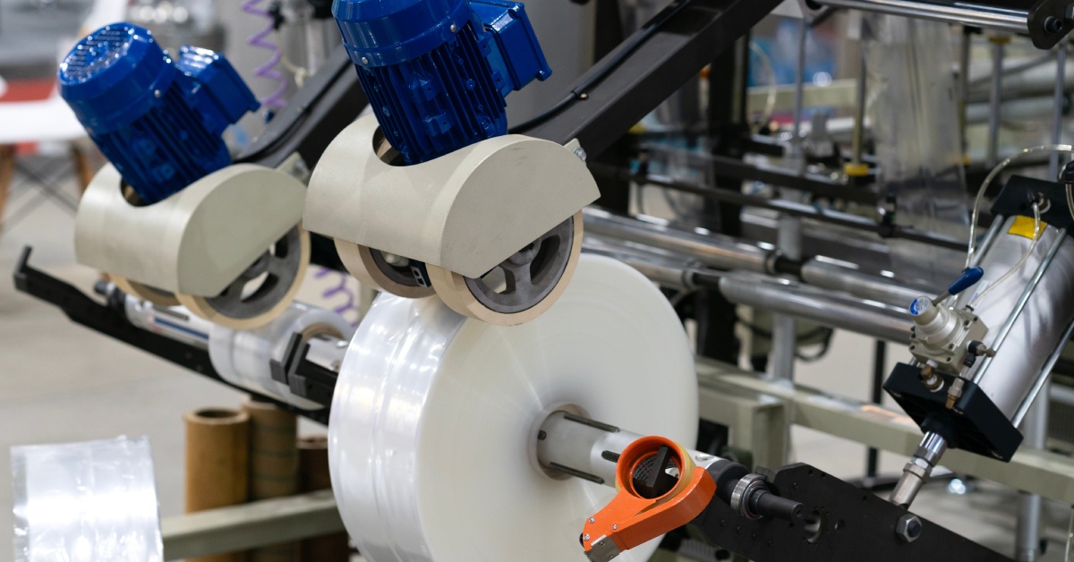 An automated food packaging machine with a spool of plastic attached to a roller in an industrial setting.