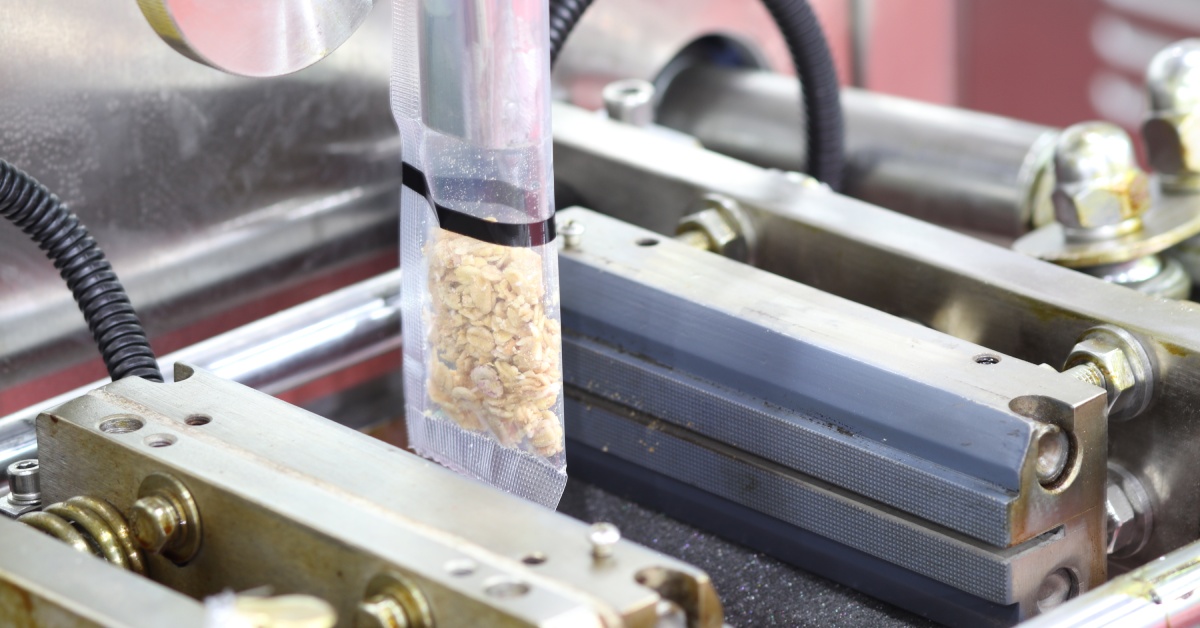 A small plastic package of food product in the process of being filled by a machine in an industrial environment.