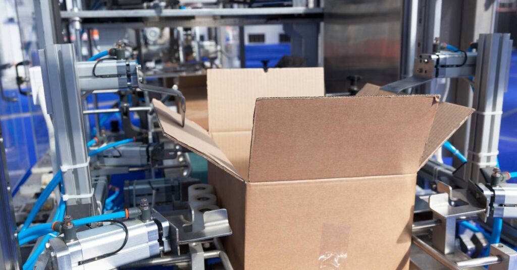 A box sitting in a packaging warehouse on a machine with knobs and rollers preparing to fill it with product.