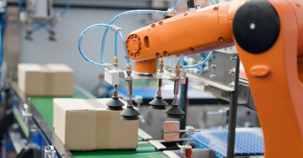 An orange machine on an assembly line using suction cups to completely seal the product packaging with tape.