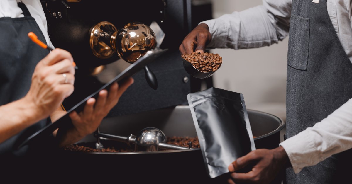 While one barista packs coffee beans into a plastic pouch, another seems to take notes in front of a roaster.