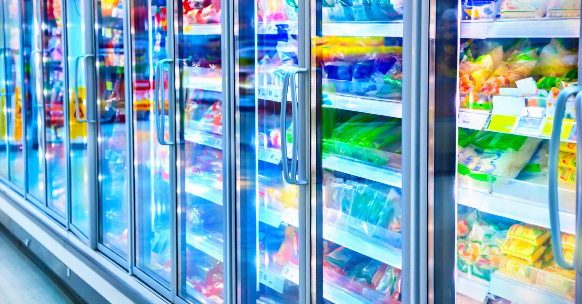 Several refrigerators in the frozen food section of a supermarket. Food products are visible through the glass doors.