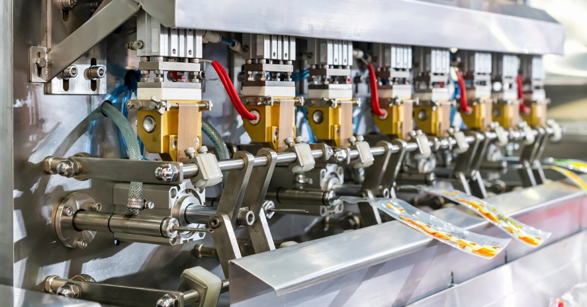 A nozzle dispenser fills several plastic pouches with a filling. The machine has colorful tubes and wiring.