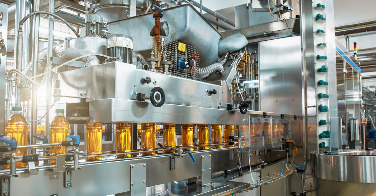 A large horizontal packaging machine with many tubes, wires, and buttons. Bottles of a yellow liquid are lined up along the belt.