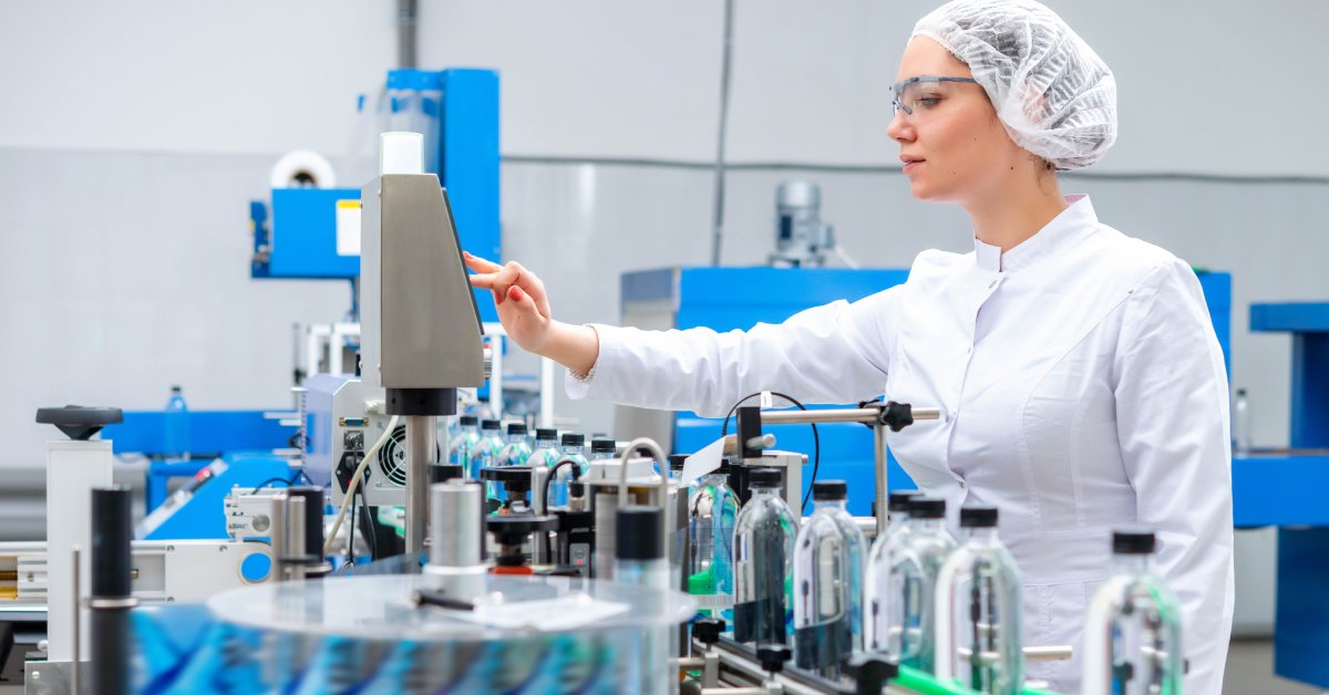 A conveyor belt moves water bottles in a line. A worker operates a device connected to the equipment.