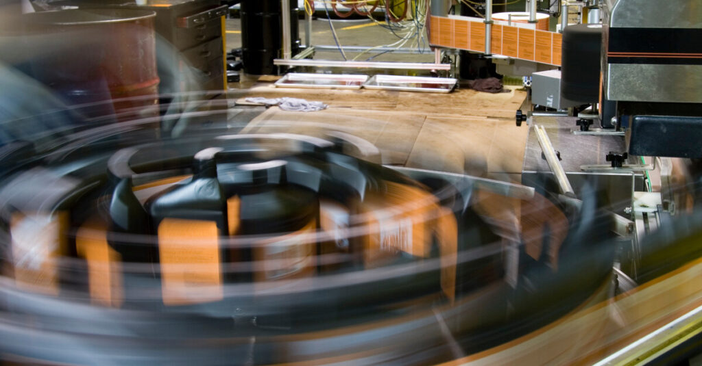 A conveyor belt rapidly moves oil products through its system in an industrial space. The action creates movement blur.