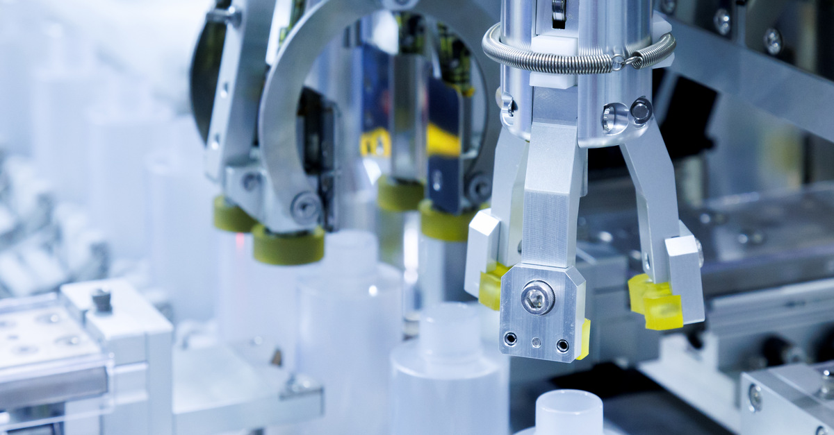 Two robotic arms place caps and labels onto plastic bottles in a production line. The environment is well lit and clean.