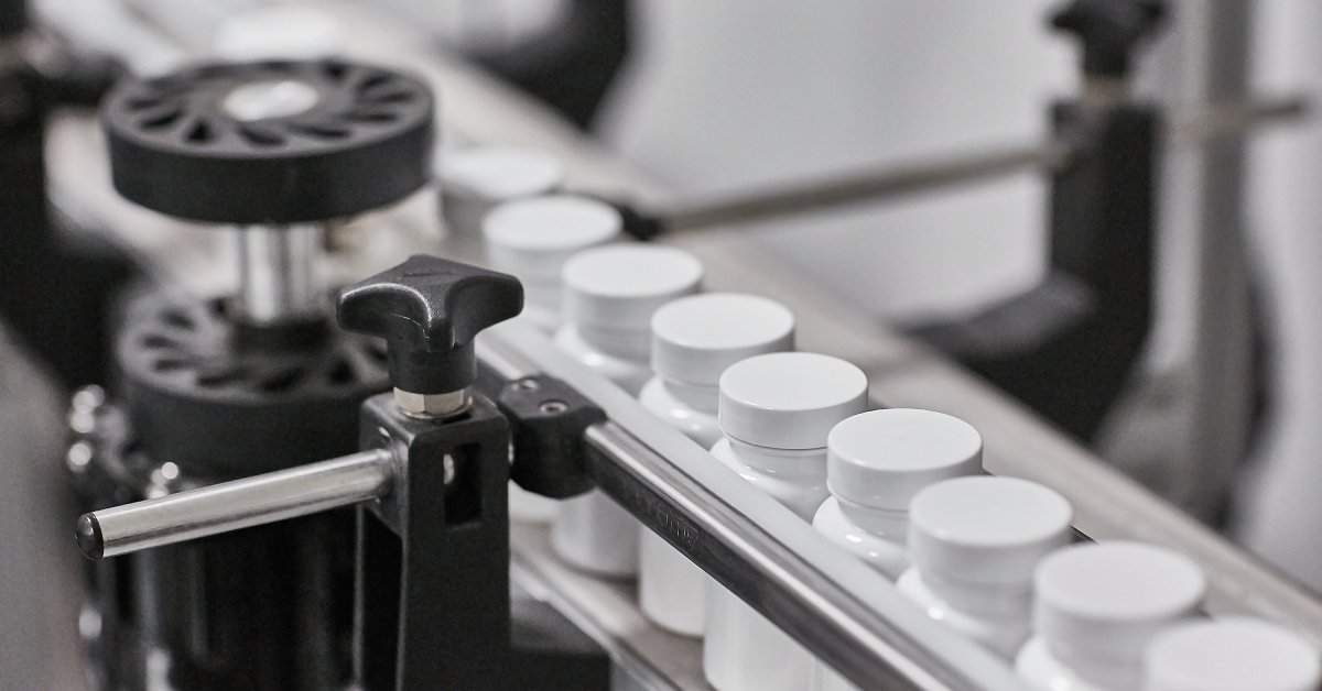 A conveyor belt system moves blank white pharmaceutical bottles through the machinery in an organized manner.